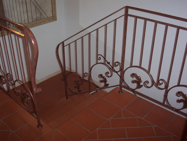 Ringhiera per scale interne in ferro lavorato, decorata con foglie e riccioli e verniciata con effetto ruggine.